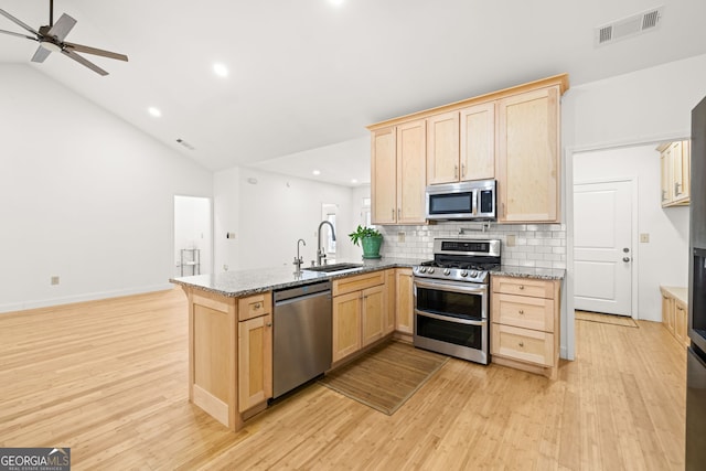 kitchen with kitchen peninsula, light brown cabinetry, light wood-type flooring, light stone countertops, and stainless steel appliances