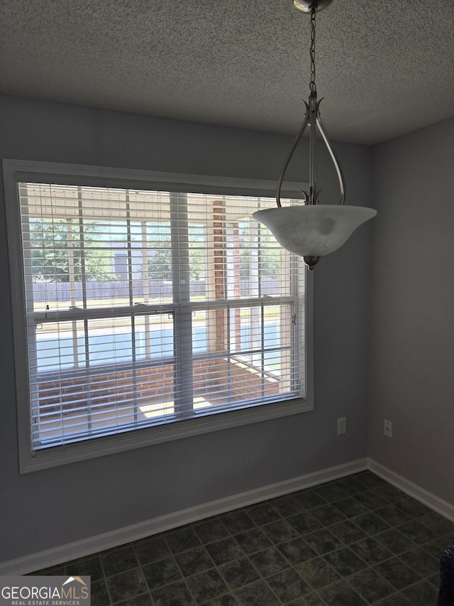 unfurnished dining area with a textured ceiling and baseboards