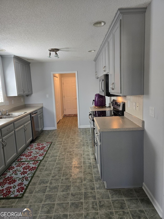 kitchen featuring stainless steel appliances, a sink, decorative backsplash, and gray cabinetry