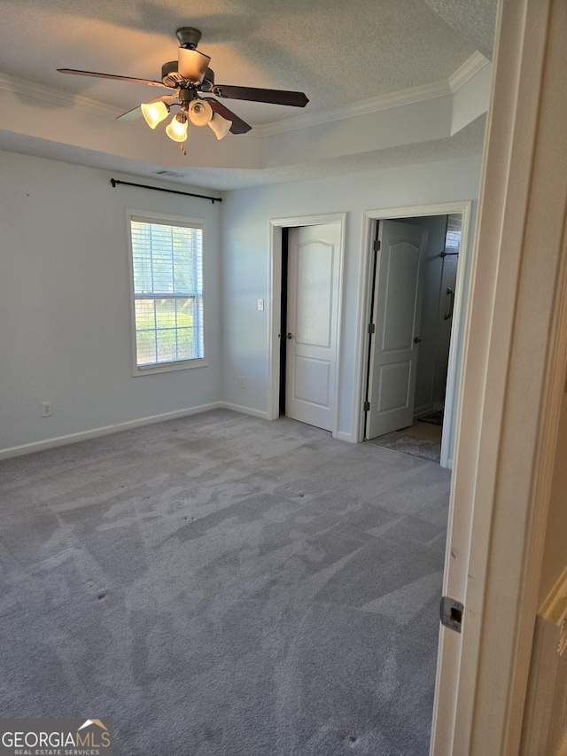 unfurnished bedroom featuring ornamental molding, a textured ceiling, a raised ceiling, ceiling fan, and carpet floors