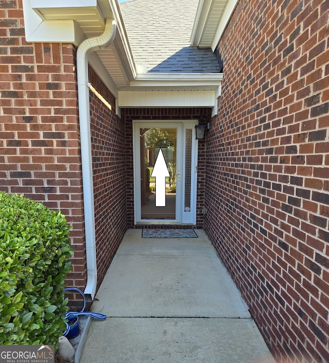 doorway to property with a shingled roof and brick siding