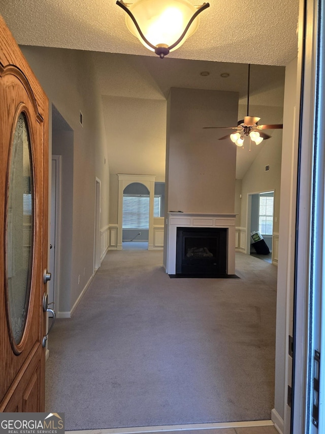 unfurnished living room featuring ceiling fan, high vaulted ceiling, carpet, and a fireplace with flush hearth