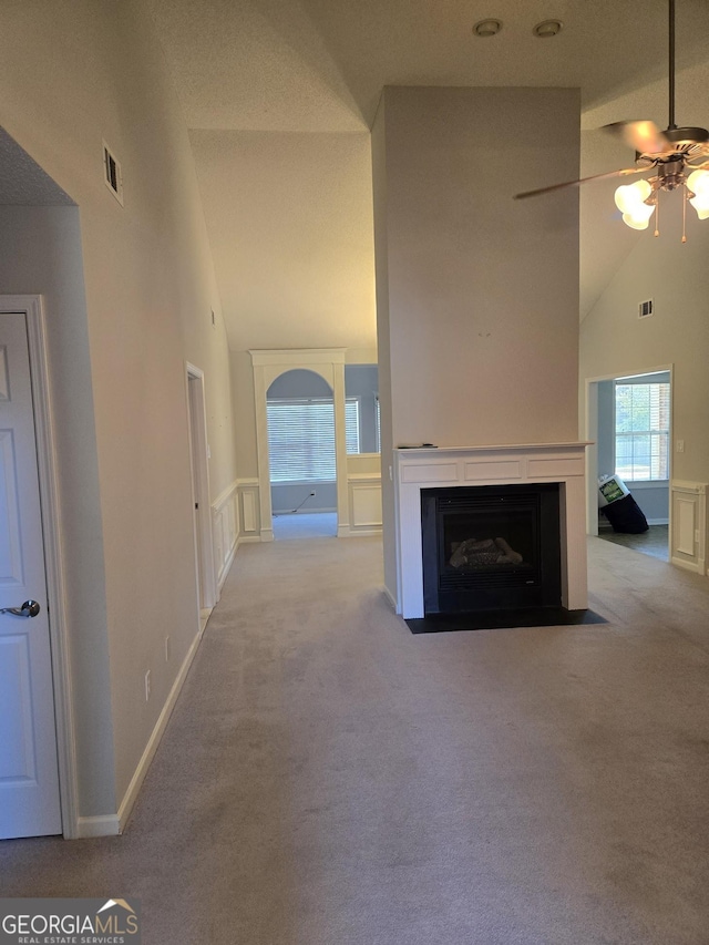 unfurnished living room featuring a fireplace with flush hearth, carpet flooring, high vaulted ceiling, and a ceiling fan