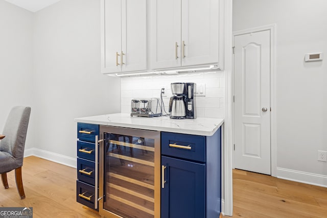 bar with backsplash, white cabinets, light wood-type flooring, blue cabinetry, and beverage cooler