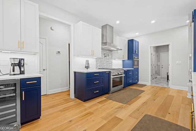 kitchen with white cabinets, wall chimney range hood, blue cabinets, wine cooler, and appliances with stainless steel finishes