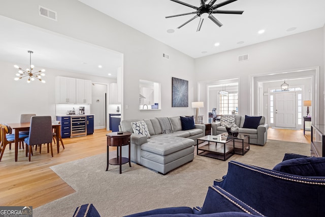 living room featuring wine cooler, a towering ceiling, light hardwood / wood-style floors, and ceiling fan with notable chandelier