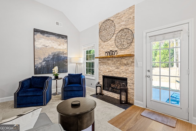 living room with a fireplace, light wood-type flooring, vaulted ceiling, and a healthy amount of sunlight