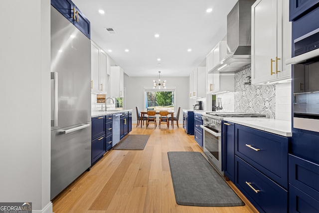 kitchen with white cabinets, premium appliances, light hardwood / wood-style flooring, and wall chimney range hood