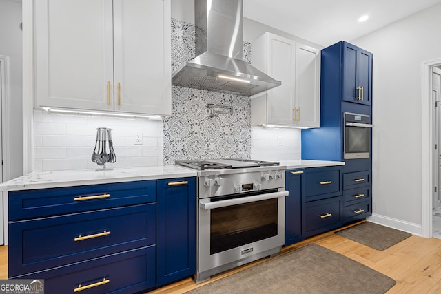 kitchen featuring white cabinets, wall chimney range hood, blue cabinets, light hardwood / wood-style flooring, and stainless steel appliances