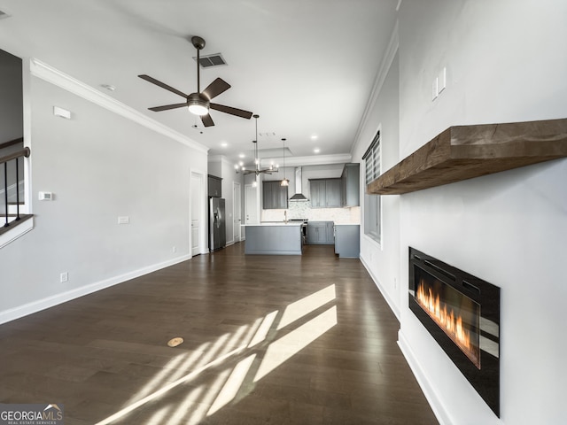 unfurnished living room featuring dark wood-style flooring, visible vents, ornamental molding, a glass covered fireplace, and baseboards