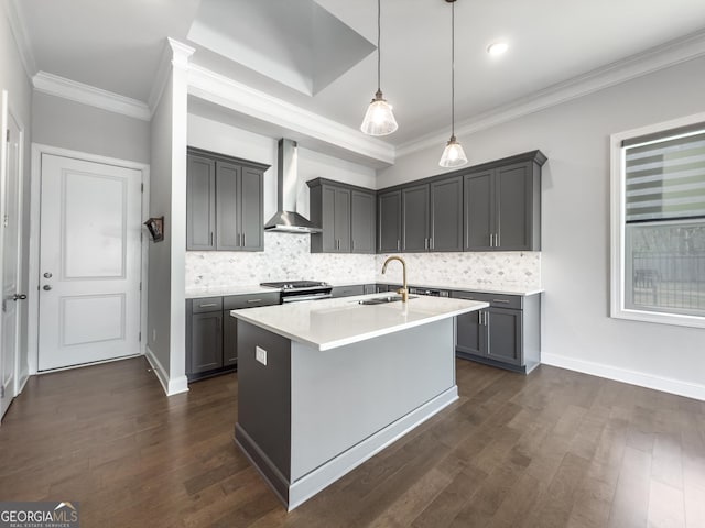 kitchen with a center island with sink, light countertops, hanging light fixtures, a sink, and wall chimney range hood