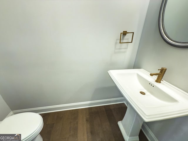 half bathroom featuring wood finished floors, toilet, and baseboards