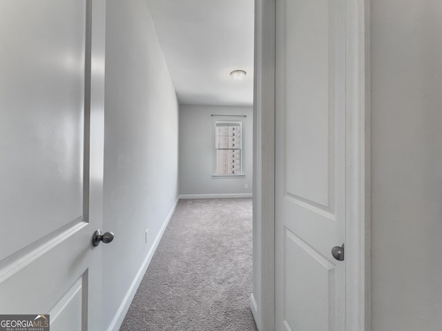 corridor with baseboards and light colored carpet