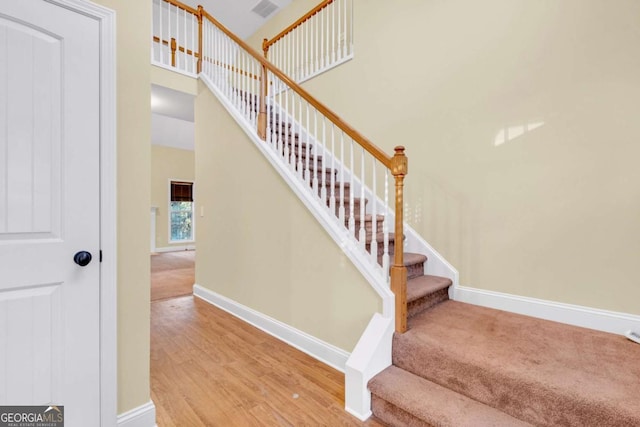 stairway with wood-type flooring and a towering ceiling