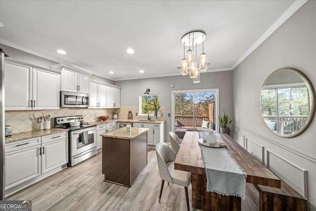 kitchen featuring stainless steel appliances, white cabinetry, hanging light fixtures, and light hardwood / wood-style floors