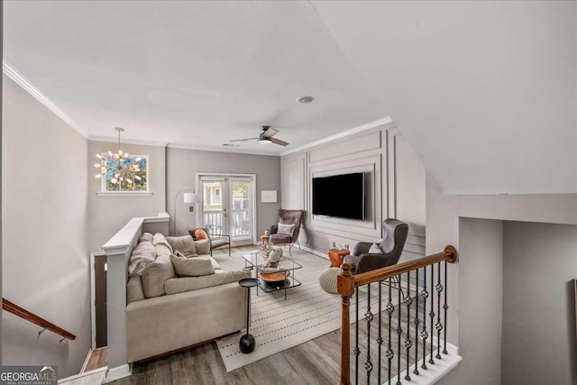 living room featuring hardwood / wood-style flooring, ceiling fan with notable chandelier, ornamental molding, and vaulted ceiling