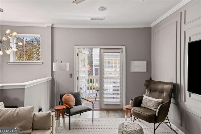 sitting room featuring plenty of natural light, light wood-type flooring, ornamental molding, and an inviting chandelier