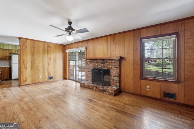 unfurnished living room featuring plenty of natural light, wood walls, a fireplace, and light hardwood / wood-style flooring