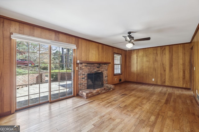 unfurnished living room with ceiling fan, a fireplace, wooden walls, and light hardwood / wood-style flooring