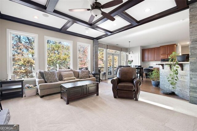 carpeted living room with plenty of natural light, ceiling fan with notable chandelier, and coffered ceiling