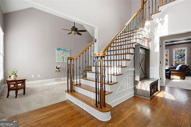 stairs with hardwood / wood-style flooring, ceiling fan, and high vaulted ceiling