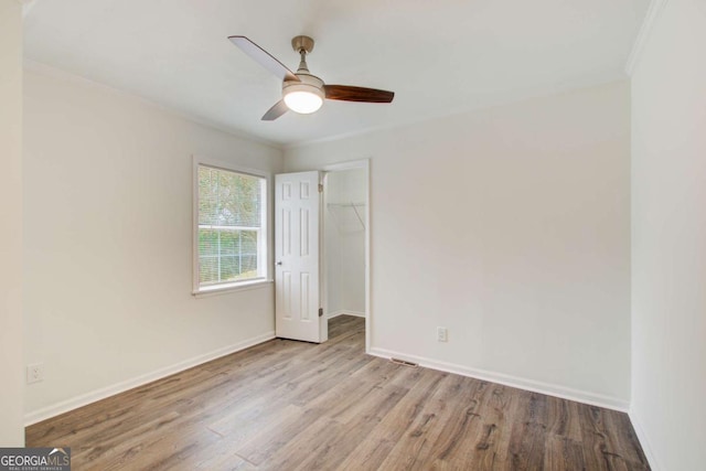 unfurnished bedroom featuring ceiling fan, a spacious closet, crown molding, a closet, and light wood-type flooring