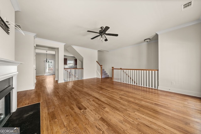 unfurnished living room with wood finished floors, a ceiling fan, visible vents, a fireplace, and ornamental molding