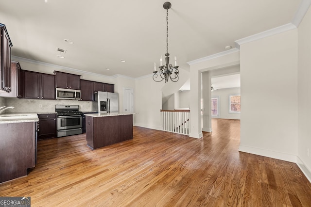 kitchen with stainless steel appliances, dark brown cabinets, light wood-style floors, backsplash, and a center island