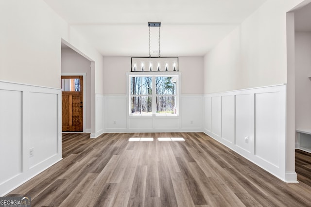 unfurnished dining area featuring wainscoting, a notable chandelier, a decorative wall, and wood finished floors