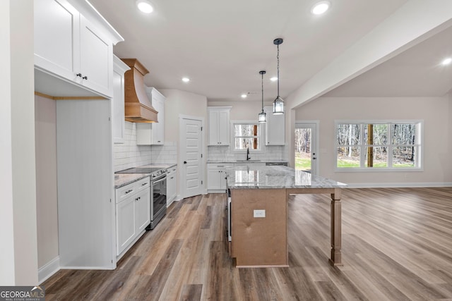 kitchen with hanging light fixtures, white cabinets, a kitchen island, light stone countertops, and stainless steel range with electric stovetop