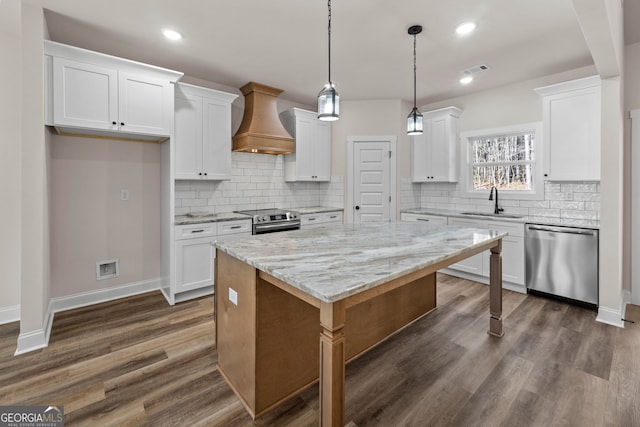 kitchen featuring a center island, stainless steel appliances, custom range hood, white cabinetry, and a sink