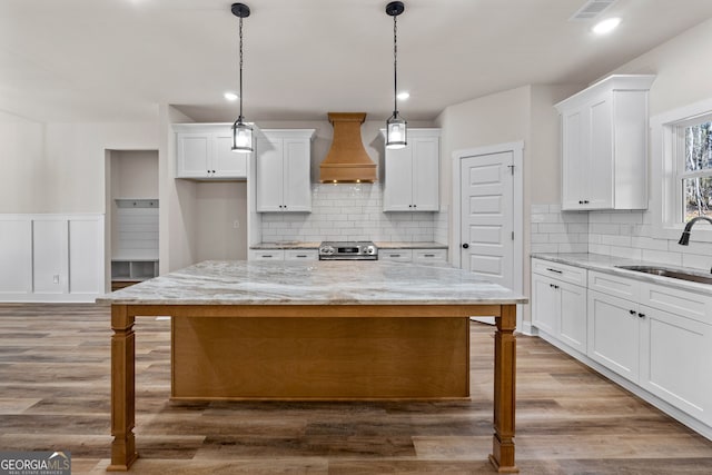 kitchen featuring a center island, white cabinetry, hanging light fixtures, and premium range hood