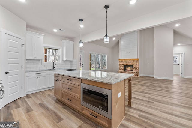 kitchen featuring built in microwave, a kitchen island, white cabinetry, hanging light fixtures, and light stone countertops