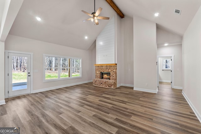 unfurnished living room featuring visible vents, wood finished floors, a brick fireplace, high vaulted ceiling, and beam ceiling