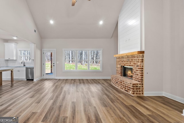 unfurnished living room with light wood-type flooring, a brick fireplace, high vaulted ceiling, and a sink