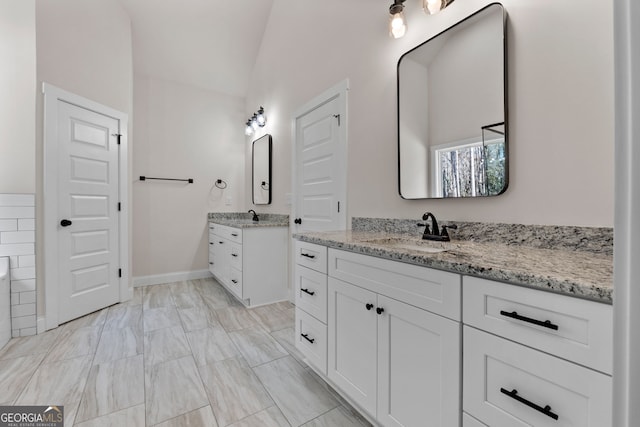 bathroom with vaulted ceiling, two vanities, a sink, and baseboards