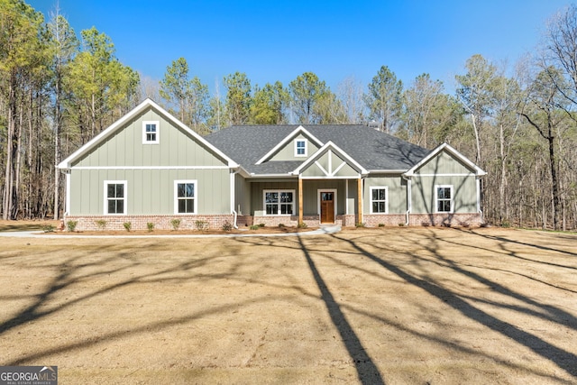 view of front facade featuring a shingled roof, board and batten siding, a porch, and brick siding