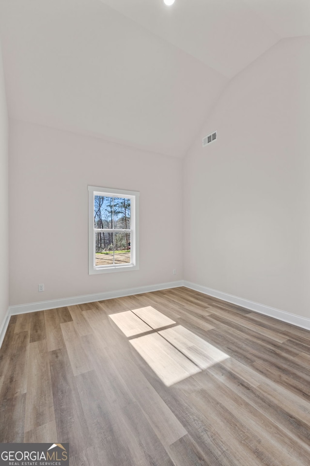 spare room with lofted ceiling, light wood-style floors, baseboards, and visible vents