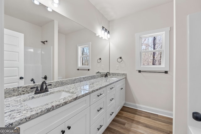 full bath featuring double vanity, a sink, baseboards, and wood finished floors