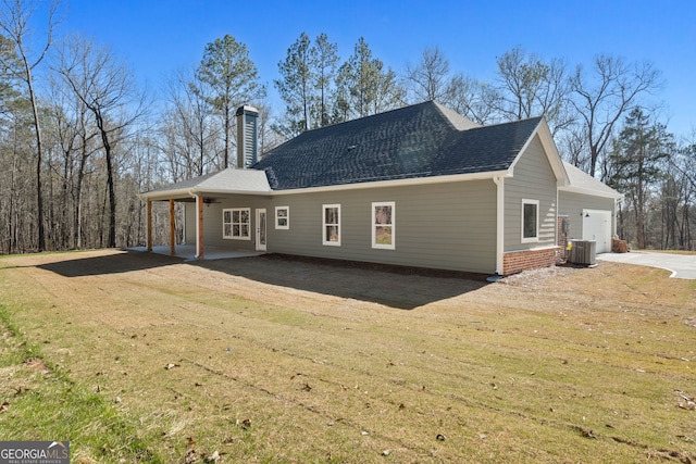 rear view of house with a garage, a shingled roof, central AC unit, a lawn, and a chimney