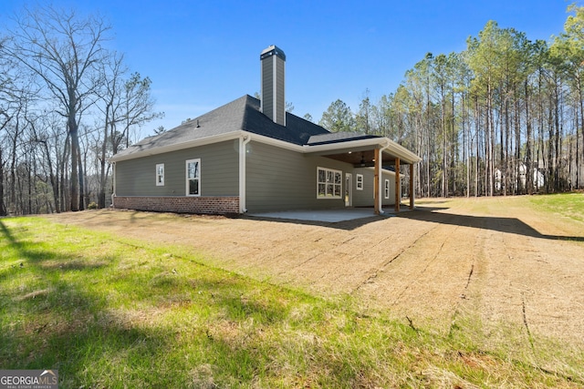 view of property exterior featuring brick siding, a yard, a patio, a chimney, and a shingled roof