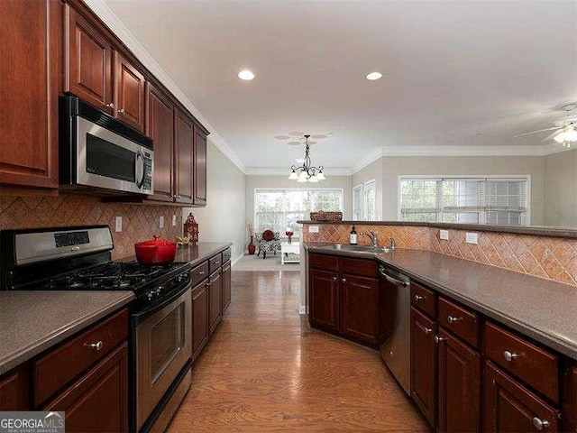 kitchen with ornamental molding, stainless steel appliances, hanging light fixtures, and light hardwood / wood-style flooring