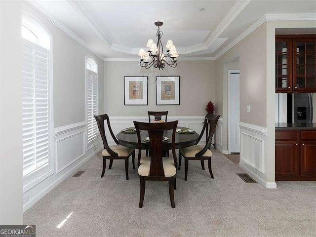 carpeted dining room featuring a raised ceiling, an inviting chandelier, and crown molding