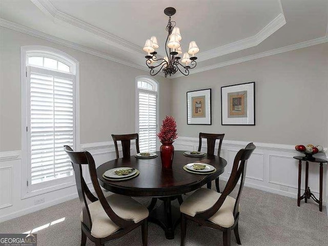 dining space with a raised ceiling, light colored carpet, an inviting chandelier, and ornamental molding