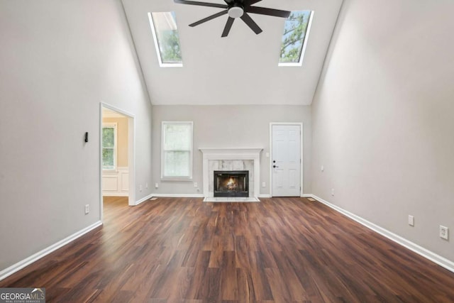 unfurnished living room featuring a skylight, a high end fireplace, dark hardwood / wood-style flooring, and high vaulted ceiling