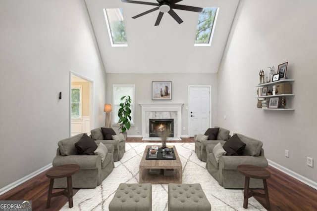 living room featuring hardwood / wood-style floors, a high end fireplace, high vaulted ceiling, a skylight, and ceiling fan