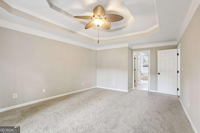 empty room featuring light carpet, a tray ceiling, ceiling fan, and ornamental molding