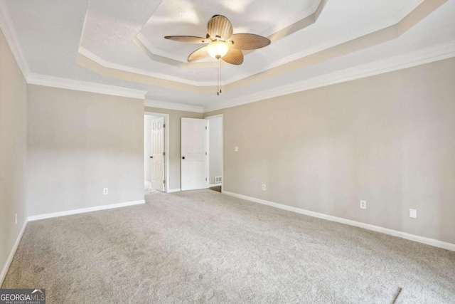 spare room featuring a raised ceiling, ceiling fan, carpet, and ornamental molding