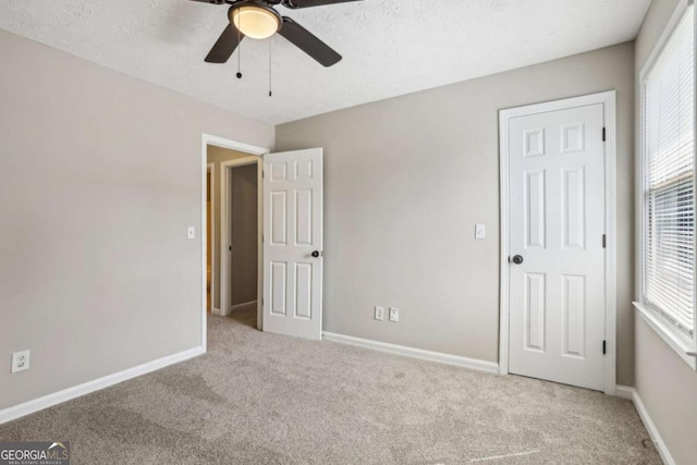 unfurnished bedroom featuring ceiling fan, light carpet, and a textured ceiling