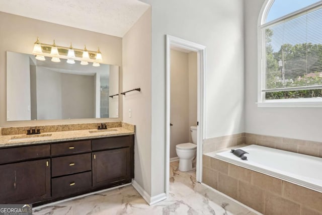 bathroom featuring vanity, toilet, a textured ceiling, and tiled tub